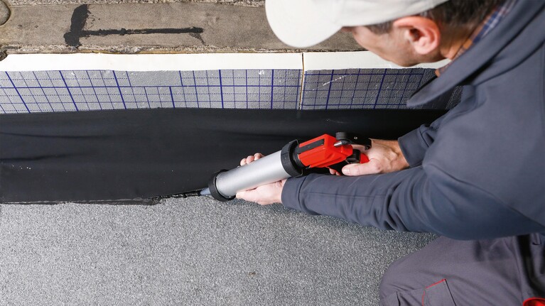 Handwerker verklebt Abdichtbahnen mit dem Folienkleber Permafix 1151 in einer Handpresspistole