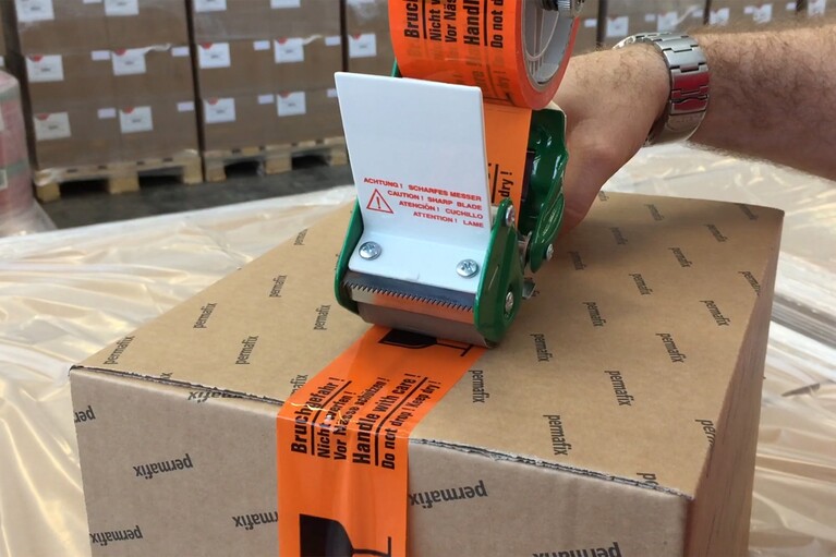 Mann verschliesst Karton mit Verpackungsklebeband vom Handabroller