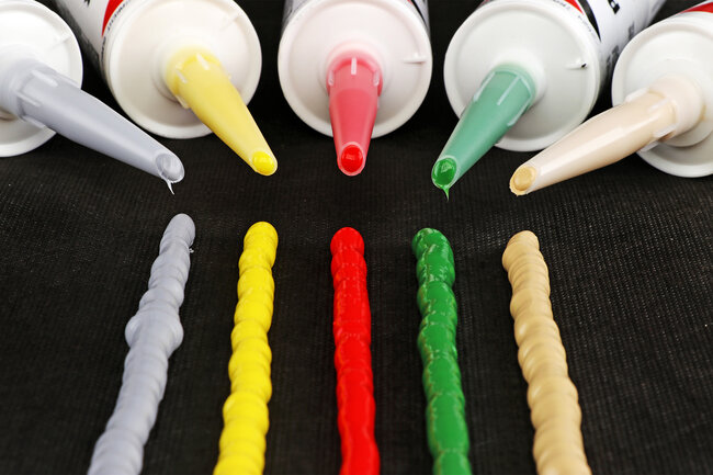 Fünf Silikonraupen in den Farben Grau, Gelb, Rot, Grün und Beige nebeneinander.