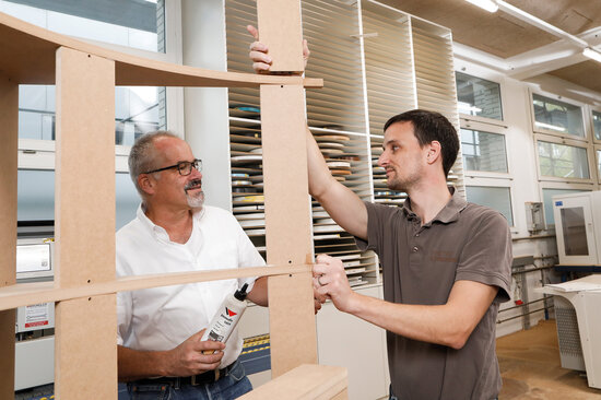 Zwei Männer vor einer frisch verklebten Holzkonstruktion.