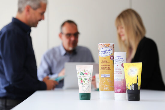 Bedruckte Mustertuben vor einer Gruppe Personen bei einer Besprechung des Pre-Production-Prozesses.