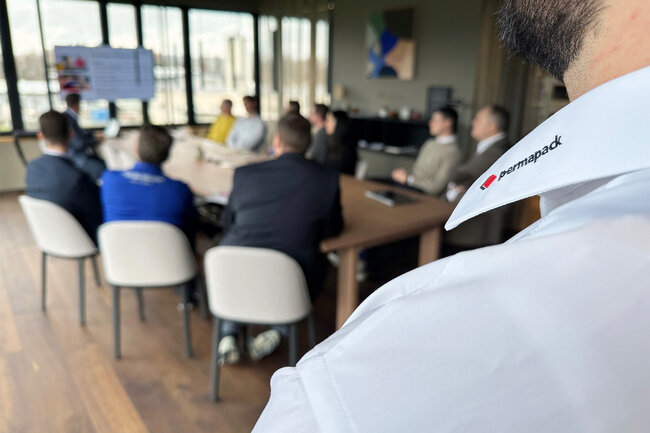 Mehrere Personen an einem Sitzungstisch, die auf einen Präsentationsbildschirm schauen. 