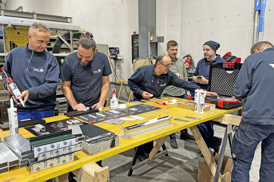 Des collaborateurs d’une entreprise de construction métallique testent des assemblages collés autour d’une table.