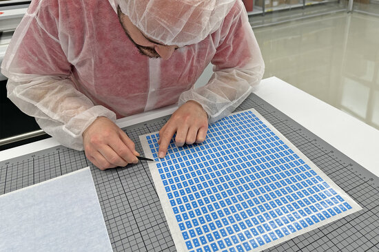 Mann mit Stanzteilen vor Plotter-Maschine