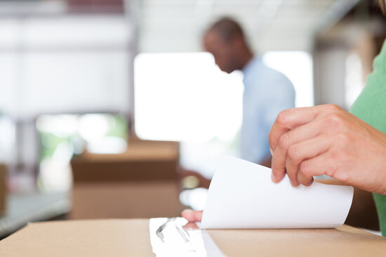 Hände, die eine Etikette auf einen Karton kleben