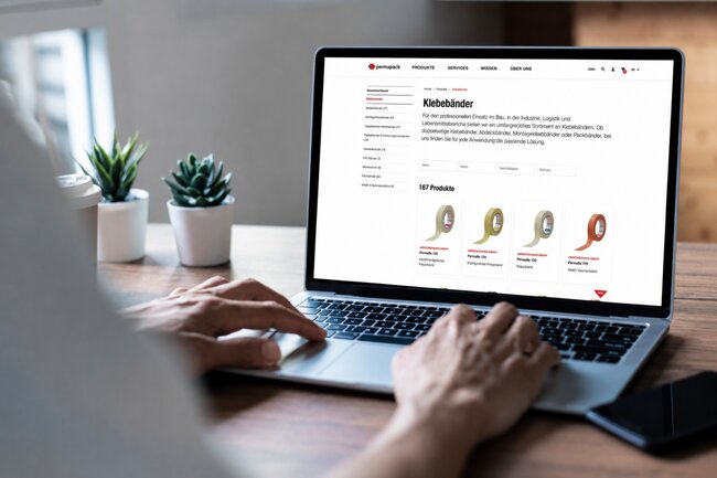 Person schaut sich über den Laptop Klebebänder im Permapack Online-Shop an