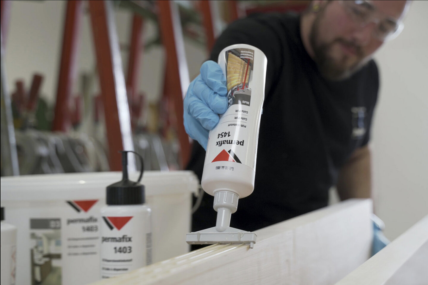 Ein Schreiner trägt transparenten PUR-Klebstoff mit einer Flächendüse auf ein Brett auf.