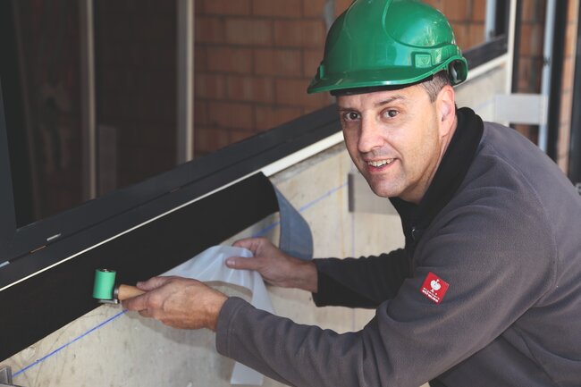 Ein Arbeiter dichtet ein Fenster auf der Wetterschutzseite mit dem selbstklebenden Abdichtungsband Permafix 455 ab.