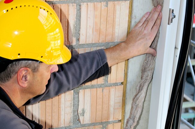 Ein Arbeiter dichtet ein Fenster mit einem Dämmzopf ab.