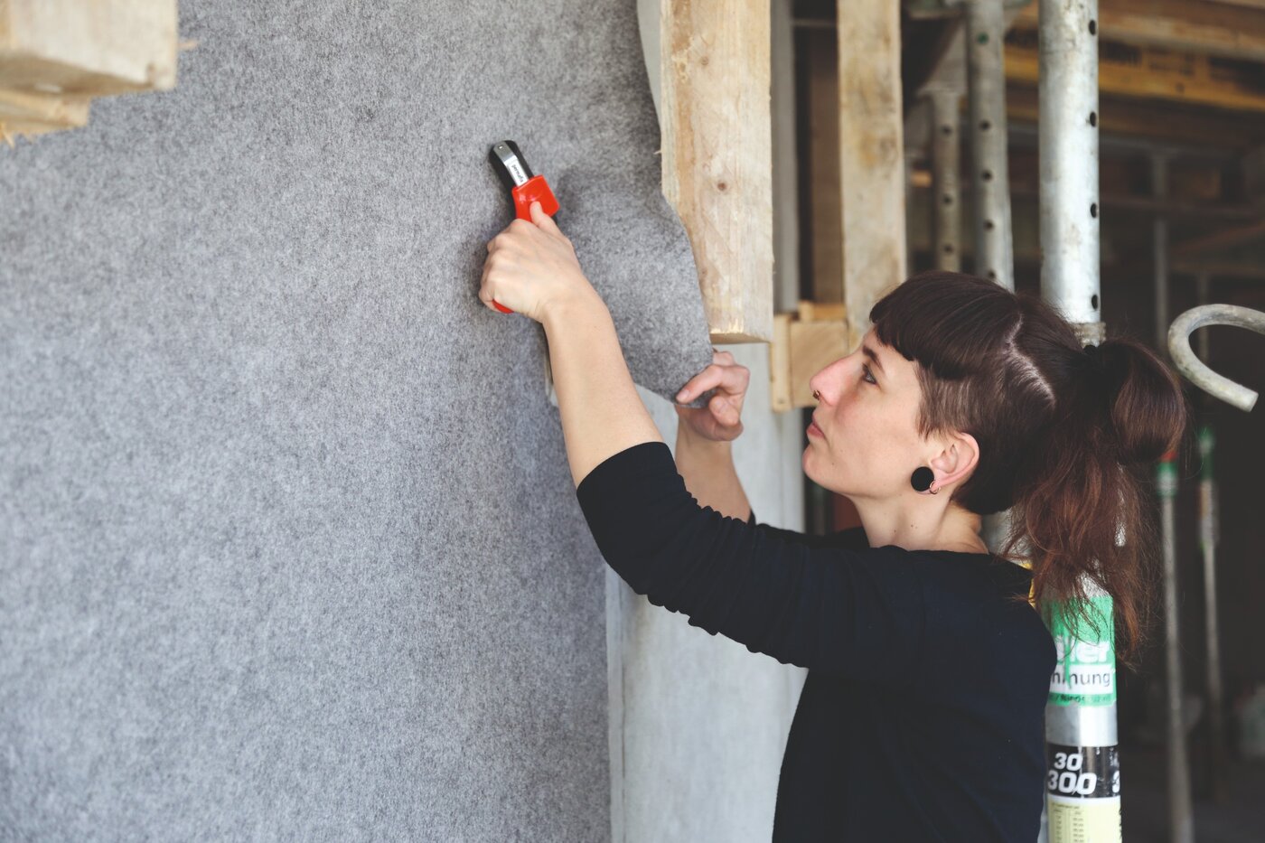 Eine Malerin verlegt das selbstklebende Schutzvlies Allfelt 1130 an einer Wand