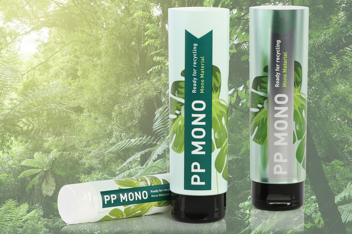 Zwei stehende und eine liegende Laminattube vor einem Hintergrund mit dichtem Blätterwald.