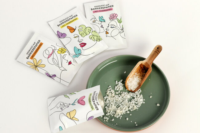 Ein Tellerchen mit Badesalz, Holzlöffelchen und einer geöffneten Barrierepapier-Verpackung 
