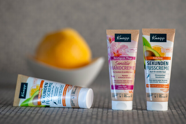 Eine liegende und zwei stehende Cremetuben mit einer Zitrone im Hintergrund.