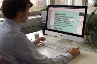 Ein Mann sitzt vor einem grosse Computerbildschirm und markiert einen Text