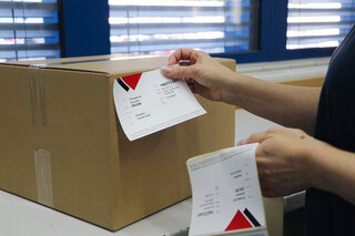 Frau klebt eine zu 100 % recycelte Etikette auf einen braune Schachtel. 