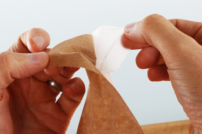Zwei Hände trennen Papier und Folie bei einem trennbaren Wickelpapier