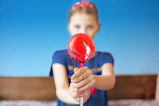 Ein Mädchen, welches einen roten Lolli hebt.
