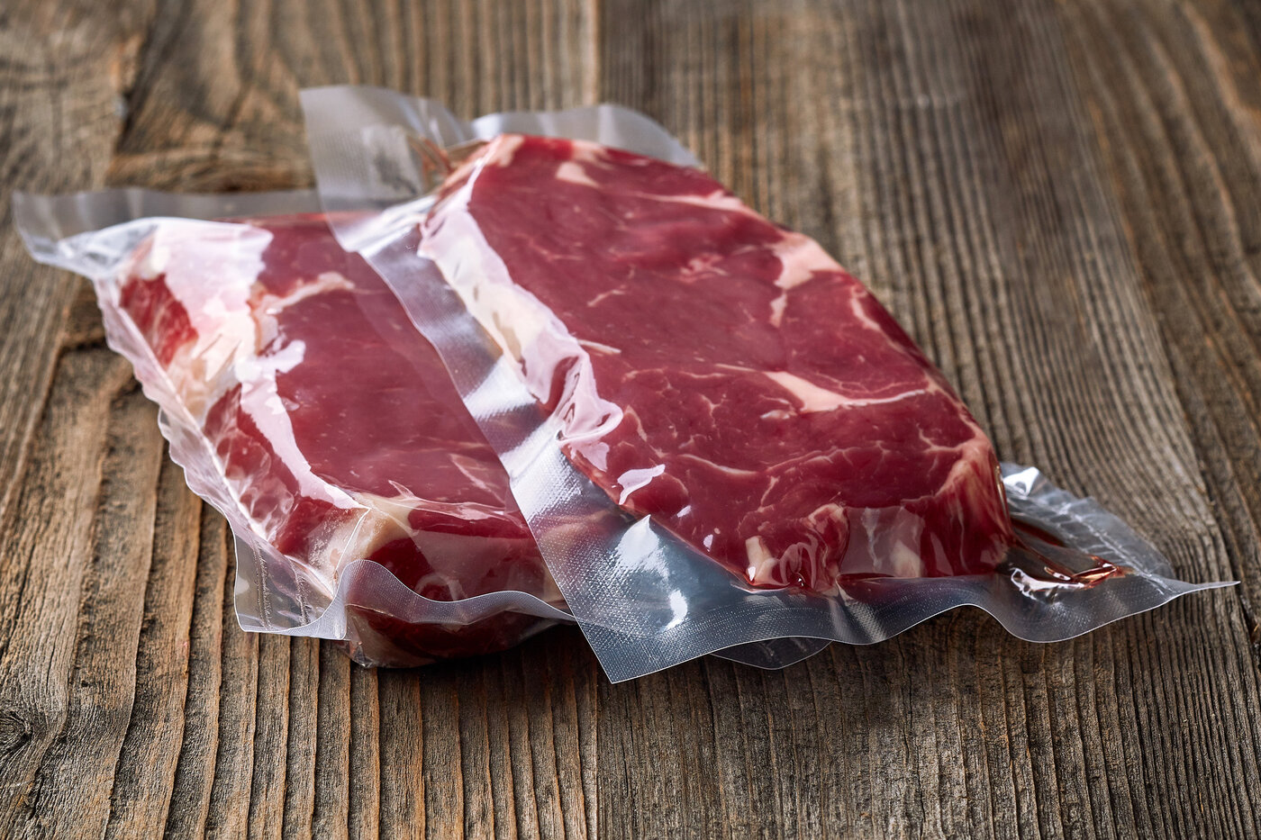 Zwei vakuumverpackte Steaks auf einem Holztisch. 