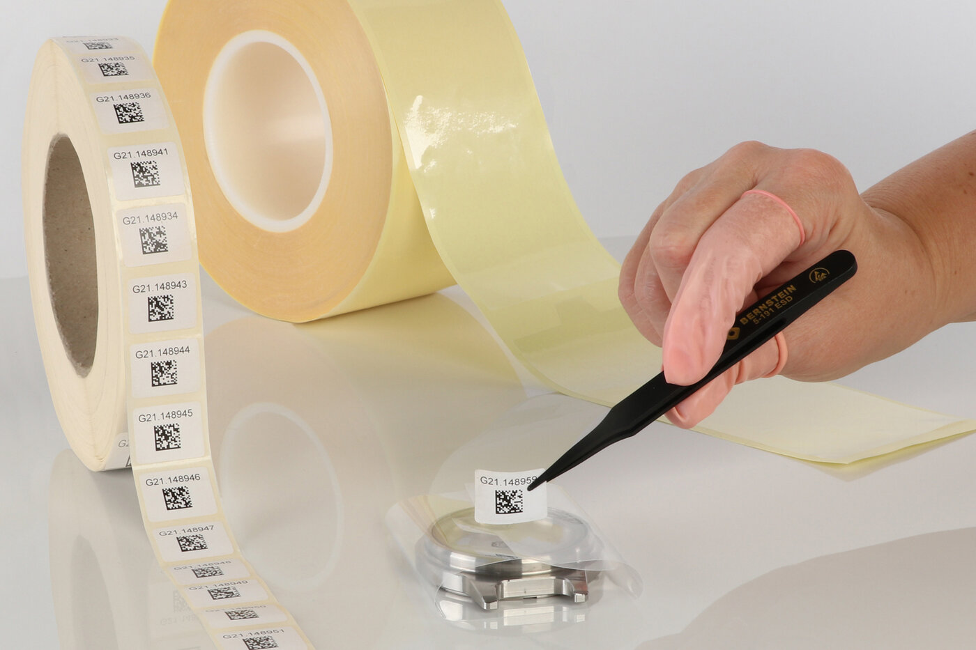 Eine Etiketten mit QR-Code wird mithilfe einer Pinzette als Verschluss auf eine Schutzfolie geklebt.