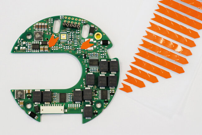 Orange Fehlerpfeile auf einer Leiterplatte und lose daneben.