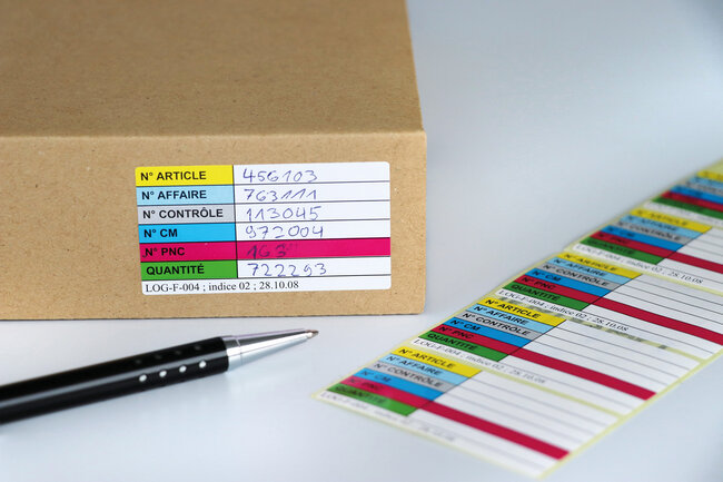 Mehrfarbig bedruckte Etiketten mit zusätzlicher Beschriftung von Hand auf einer Schachtel und lose daneben. 