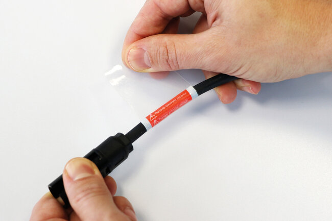 Eine laminierte Etikette wird auf ein Kabel aufgeklebt. 