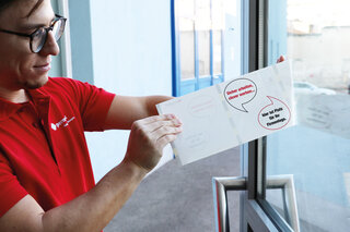 Mann klebt eine Fensteretikette auf eine Türscheibe.