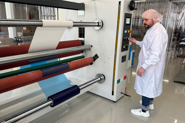 Mann bedient in weisser Schutzbekleidung eine Kaschieranlage mit blautransparenter Oberflächenschutzfolie.