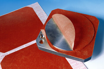 Rote Formstanzteile auf einem Bogen und auf einem Metallstück. 