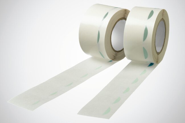 Runde, transparente Formstanzteile mit grüner Anfasslasche auf einer Rolle