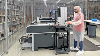 Mann in weisser Schutzbekleidung bedient in einem Reinraum eine Maschine.