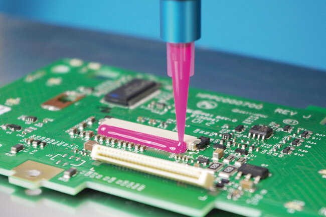 Une chenille de colle rose fixe des composants sur un circuit imprimé vert. 