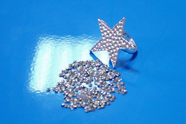 Fingerring mit Sternaufsatz mit Vertiefungen, davor viele Strasssteine. 