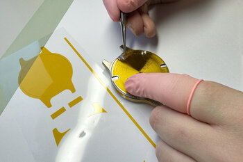 Polyimid-Formstanzteil wird auf Uhrenboden aufgebracht. 