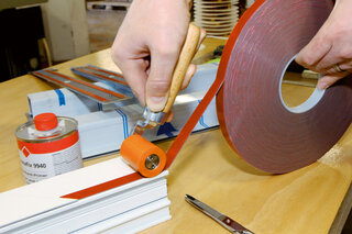 Klebeband wird mit einem Anpressroller auf ein Kunststoffteil angepresst. 