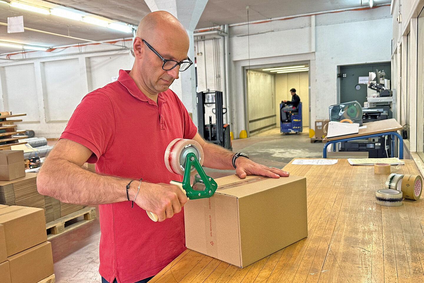 Mitarbeiter verschliesst einen Karton mit einem nachhaltigen Paketband aus recyceltem PP.