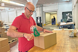 Mitarbeiter verschliesst einen Karton mit einem nachhaltigen Paketband aus recyceltem PP.