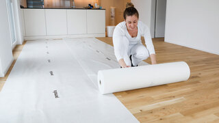 Weiss gekleidete Frau rollt weisses Abdeckvlies aus