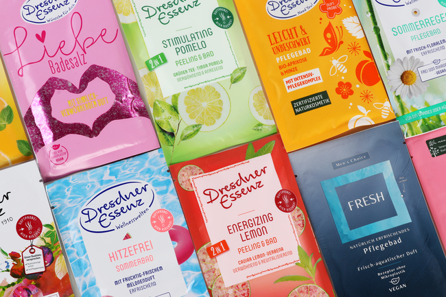Mehrere Sachet-Verpackungen für Bade- und Pflegeprodukte in verschiedenen Farben und Designs, angeordnet auf einer ebenen Fläche