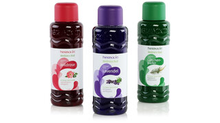 Drei Flaschen Wellness-Bad mit rot, violett und grün bedruckten Dekorationsetiketten der Marke Herbacin. 