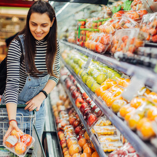 Au rayon des fruits et légumes, une femme place dans son caddie une barquette de pommes emballée dans un film extensible. (