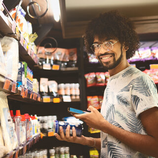 Ein Mann hält in der Convenience-Abteilung ein Produkt und ein Mobiltelefon in den Händen.