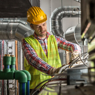 Ein Mann mit Helm umgeben von Lüftungsrohren.