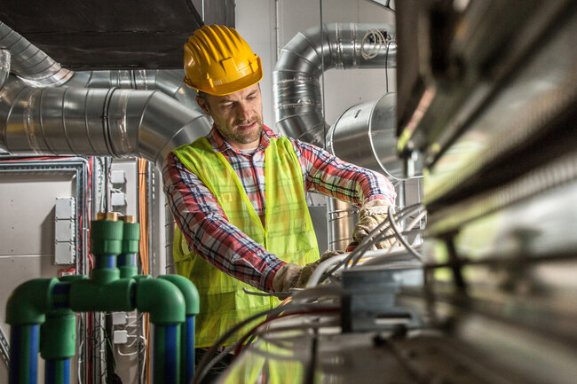 Ein Mann mit Helm umgeben von Lüftungsrohren.