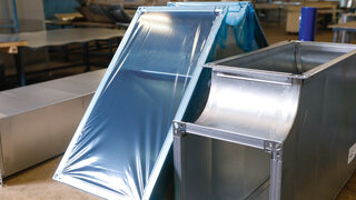 Ein Bauteil für einen Lüftungskanal ist bedeckt mit einer blautransparenten Oberflächenschutzfolie. 