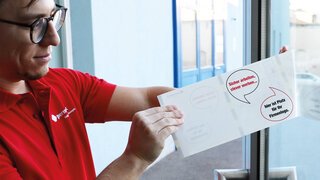 Mann klebt eine Fensteretikette auf eine Türscheibe.