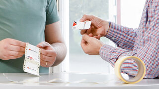 Zwei Männer halten Etiketten mit Sicherheitsmerkmalen und Blindenschrift in den Händen. 