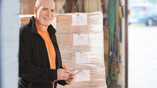 Mann steht vor einer Palette mit gestretchten Kartons.