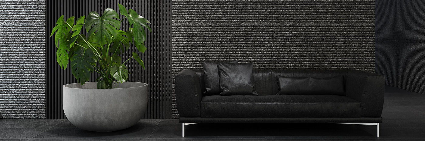 Betonfarbenes, rundes Pflanzengefäss der Marke Cosapots mit einer Monstera-Pflanze vor einer dunklen Wand