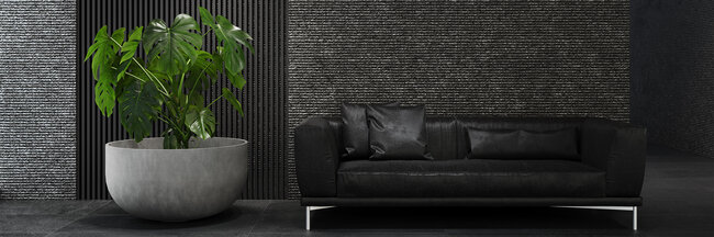 Betonfarbenes, rundes Pflanzengefäss der Marke Cosapots mit einer Monstera-Pflanze vor einer dunklen Wand